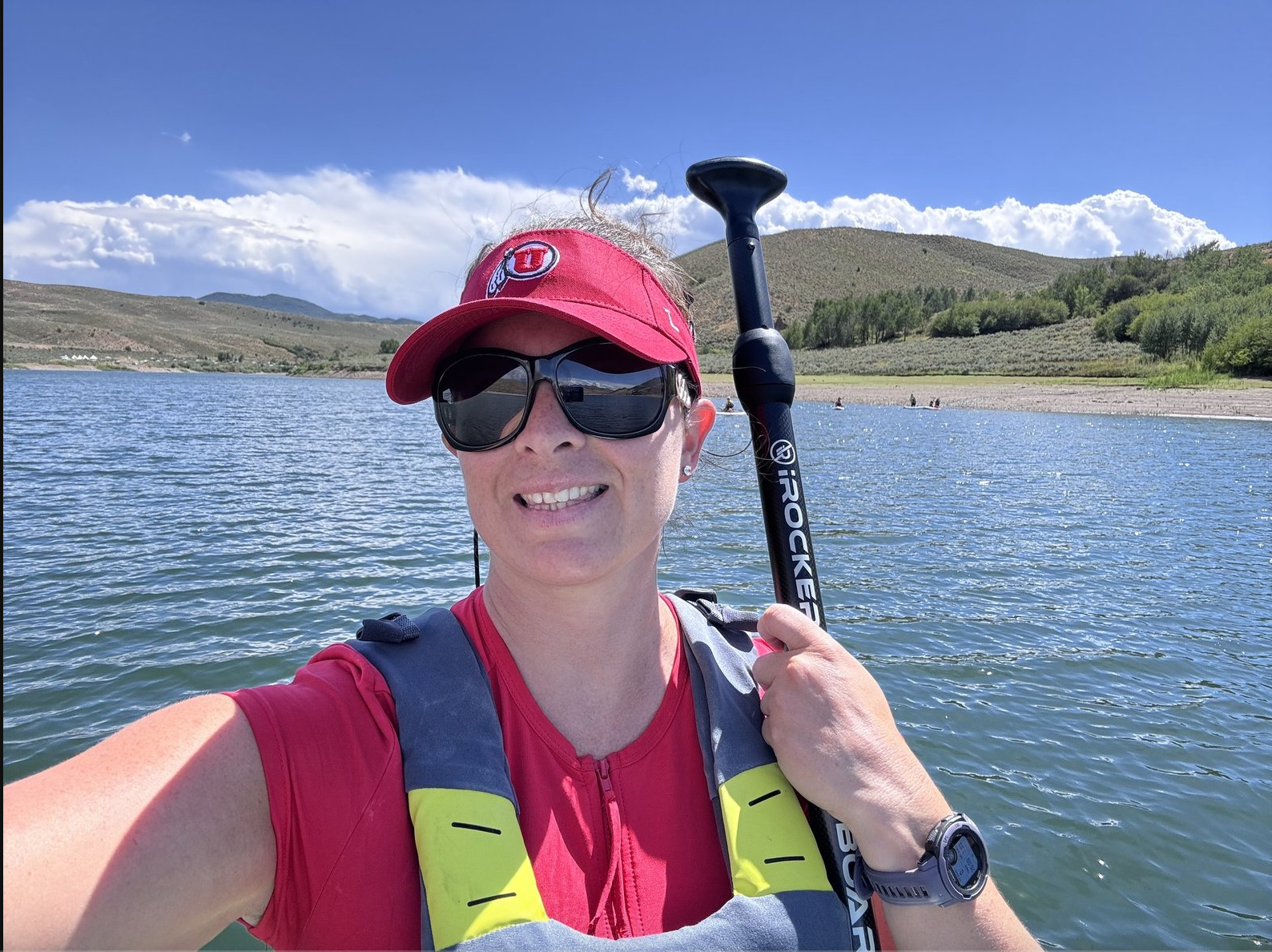M. Spring wearing sunglasses and holding a paddle on a mountain lake